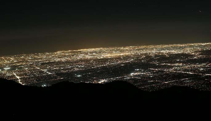 Nighttime view from a mountain peak overlooking the sprawling, brightly lit carpet of Los Angeles city lights.