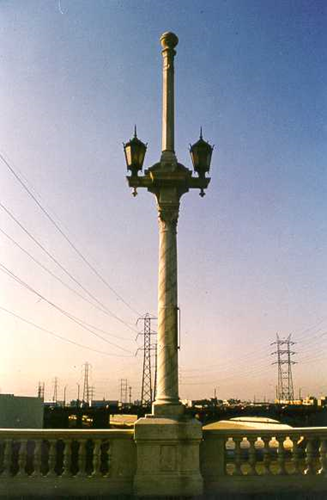 Historic bridge lamp post with a tall central spire and two flanking lanterns on a stone balustrade.