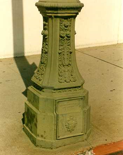 Close-up shot of an ornate green metal lamp post base featuring intricate floral relief carvings and a square access panel.