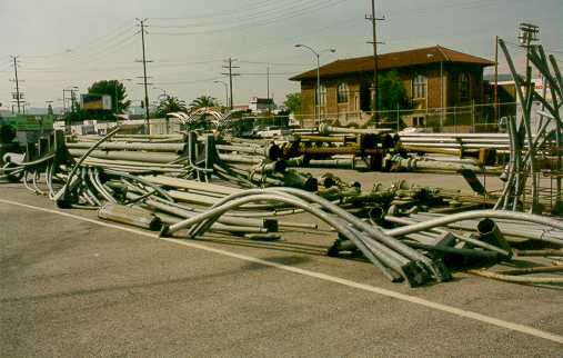 Long, curved metal street lighting poles stacked horizontally in a maintenance yard.
