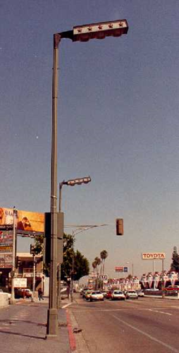 Industrial street lamp with a rectangular horizontal light fixture near a busy intersection.