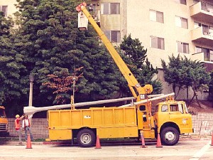 A yellow utility bucket truck with an extended boom arm being used by a worker to service a streetlight.