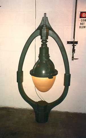 An industrial pendant light featuring a bulbous globe hanging within a dark oval metal frame.