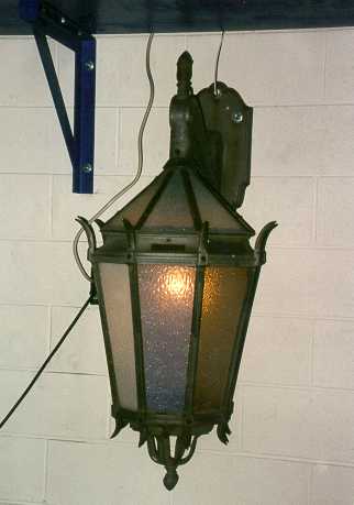 A six-sided gothic style lantern with textured glass, hanging from a wall-mounted bracket.