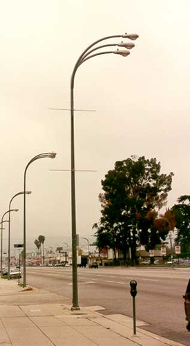 Tall street lamp with three arched horizontal arms positioned over a wide road.