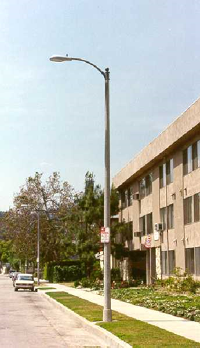 Slim grey streetlight standing on a sidewalk next to a multi-story apartment building.