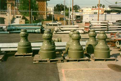 Several decorative green metal lamp post bases sitting on wooden pallets in an outdoor yard.